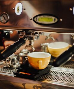 Espresso machine brewing a fresh coffee into a yellow cup in a cafe setting.